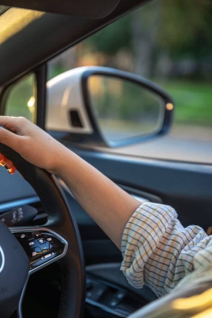 Young woman driving a car. Hands on the wheel. Side mirror in the car.